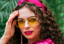 Bold Tropical Makeup Trends to Try Caucasian model with bright crimson lipstick and headband posing against a backdrop of palm leaves.