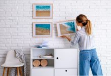Beach Style Home Décor for Inspired Tropical Living An interior decorator hangs artworks of beach scenes on a white wall in a tropical home.