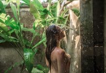 Open Showers Are a Way to Connect with Nature Young woman showering in an open shower in the tropics with tropical plants growing inside the shower.