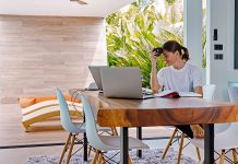 Best Tile Flooring Types for Tropical Homes Woman sitting at table in front of open sliding doors leading onto a terrace in a tropical house.