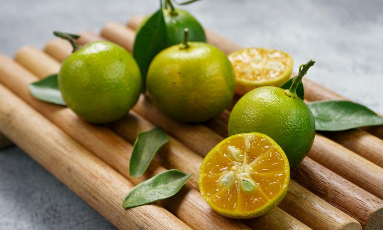 Five ripe calamansi fruit on a bamboo tray with one cut open to show the juicy inside.