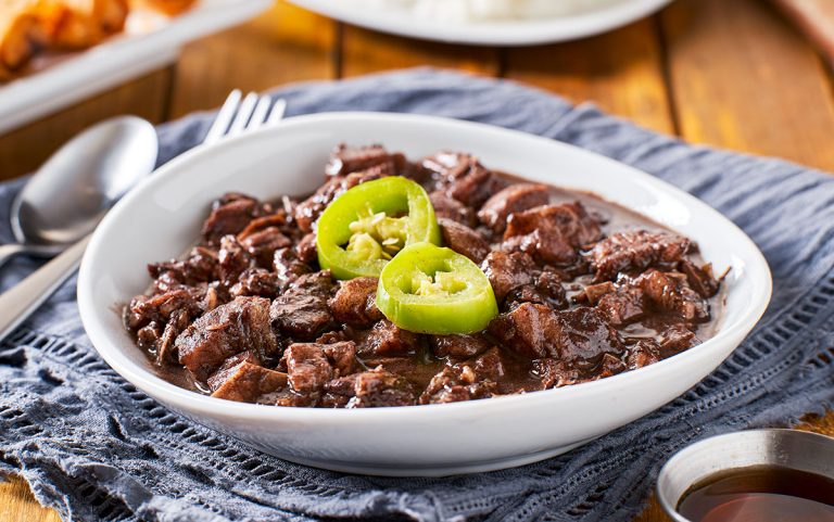 A white bowl on a table containing Filipino pork blood stew known as dinuguan garnished with two slices of green chili pepper.