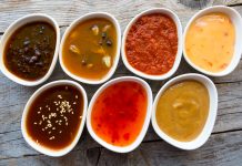 Some Pungent Condiments from Southeast Asia to Try Close-up view of seven white bowls containing different Southeast Asian condiments on a wooden table.